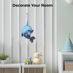 Decorative blue whale wall hanging in a room with a plant and small table.