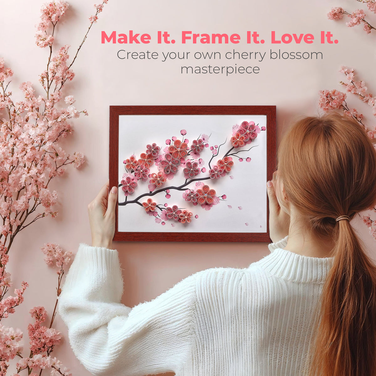 Woman holding a framed cherry blossom artwork with text 'Make It. Frame It. Love It.' on a pink background.