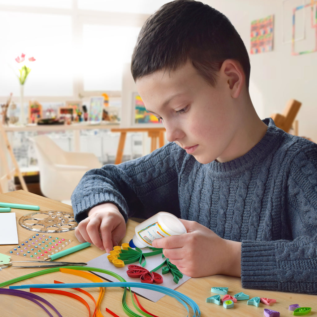 Child engaged in arts and crafts activity with colorful materials on a table.
Child using a slotted quilling tool to create rolled paper designs for greeting cards