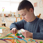 Child engaged in arts and crafts activity with colorful materials on a table.
Child using a slotted quilling tool to create rolled paper designs for greeting cards