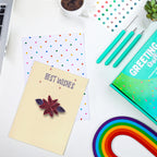 Greeting card with 'Best Wishes' and decorative pin, surrounded by stationery items on a white surface.
DIY paper quilling greeting card with quilling tools, colorful paper strips, and craft supplies