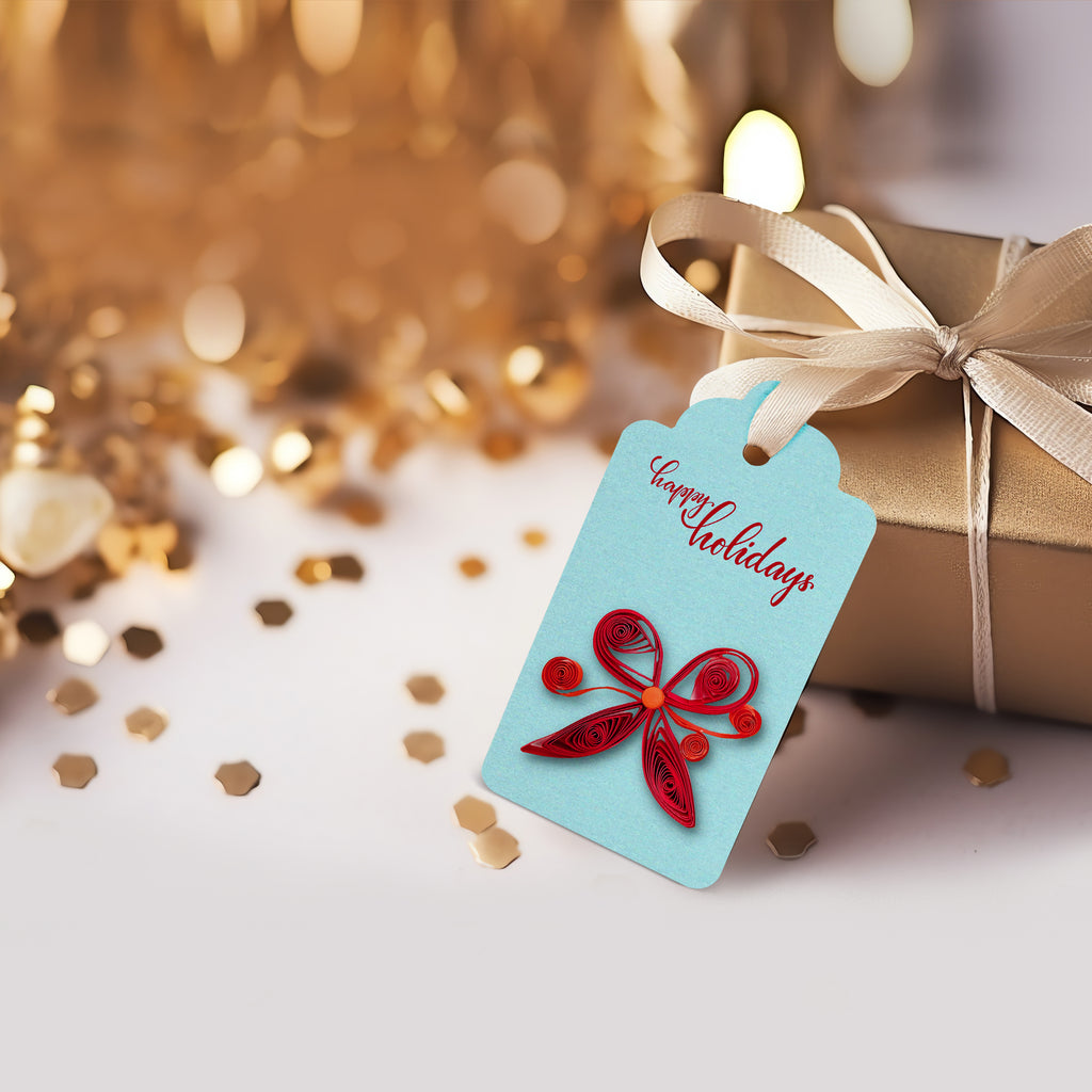 Gift with a blue tag featuring a red butterfly design and 'Happy Holidays' text, surrounded by gold confetti.
Handmade gift tag decorated with paper quilling flowers and embellishments