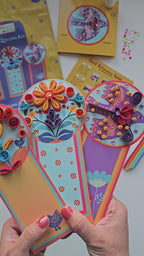 Hands holding completed folklore quilled bookmarks, showing colorful finished designs.
