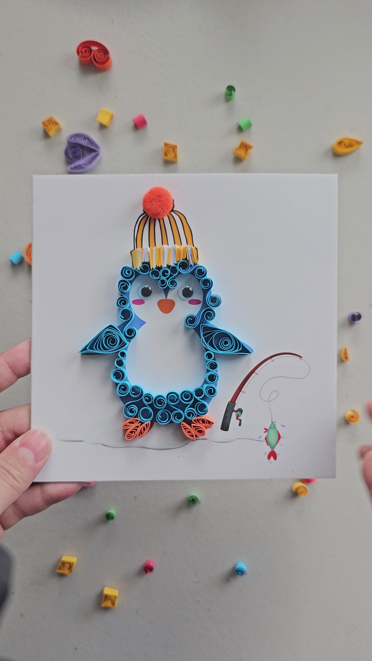 Hands creating a penguin paper quilling artwork using an intermediate DIY craft kit
